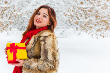 beautiful smiling woman holding a gift box on a snowy forest background