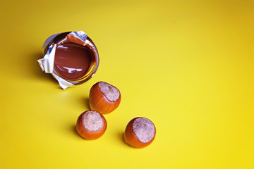 Three unpeeled hazelnuts and a jar of chocolate paste on a yellow background. Flatley.