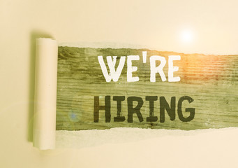 Handwriting text We Re Hiring. Conceptual photo process of reviewing applications and finding candidates Cardboard which is torn in the middle placed above a wooden classic table