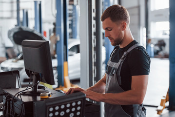 Professional mechanic. Man at the workshop in uniform use computer for his job for fixing broken car