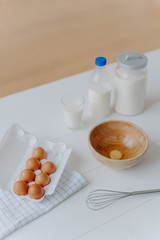 Top view of different dough recipe ingredients at kitchen table. Eggs, whisk, glass of milk and flour. Cooking, baking and culinary concept.