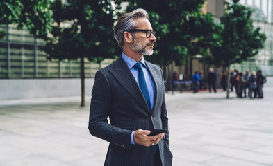 Serious mature businessman with smartphone at street