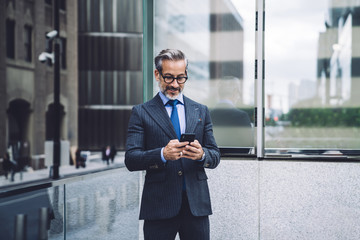 Mature male in elegant suit typing on smartphone