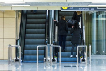 People on the escalator or moving staircase with inscription departure in English and Chinese in the international airport or railway station from the back moving upstairs with luggage