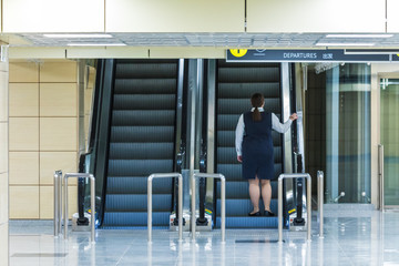 The alone woman on the escalator or moving staircase with inscription departure in English and Chinese in the international airport or railway station from the back moving upstairs with luggage