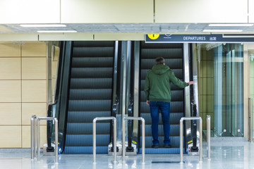 The alone man on the escalator or moving staircase with inscription departure in English and Chinese in the international airport or railway station from the back moving upstairs with luggage