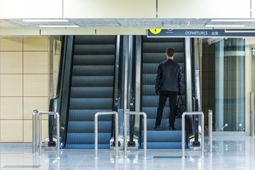 The alone man on the escalator or moving staircase with inscription departure in English and Chinese in the international airport or railway station from the back moving upstairs with luggage