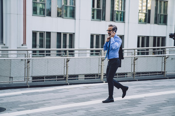 Mature businessman talking on phone and walking on street