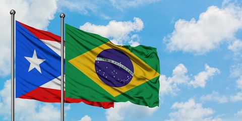 Puerto Rico and Brazil flag waving in the wind against white cloudy blue sky together. Diplomacy concept, international relations.