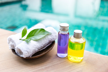 Spa concept background, Massage oil in glass bottle with white hand towel on swimming pool edge with space on blurred blue water background, outdoor day light
