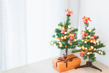 Two small Christmas trees decorated with lights And the gift box on a wooden table that is placed in the corner of the room.