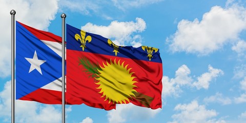 Puerto Rico and Guadeloupe flag waving in the wind against white cloudy blue sky together. Diplomacy concept, international relations.