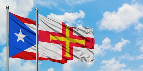 Puerto Rico and Guernsey flag waving in the wind against white cloudy blue sky together. Diplomacy concept, international relations.