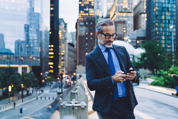 Mature thoughtful male using mobile on urban background