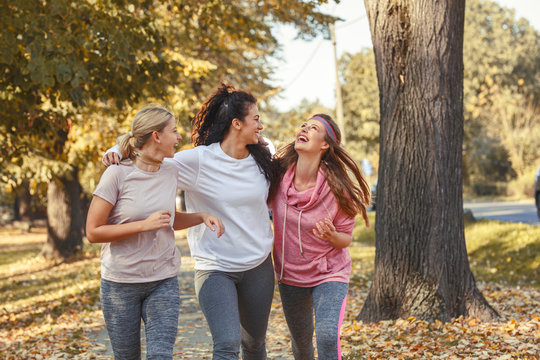 Group of female friends jogging at the city park.Relaxing after running and making fun.Autumn season.	