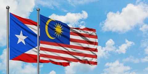 Puerto Rico and Malaysia flag waving in the wind against white cloudy blue sky together. Diplomacy concept, international relations.