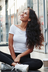 Vertical photo. Beautiful woman with curly black hair have good time in the city at daytime
