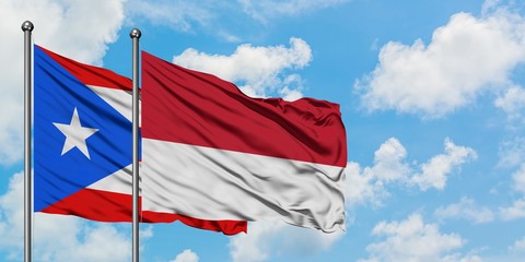 Puerto Rico and Monaco flag waving in the wind against white cloudy blue sky together. Diplomacy concept, international relations.