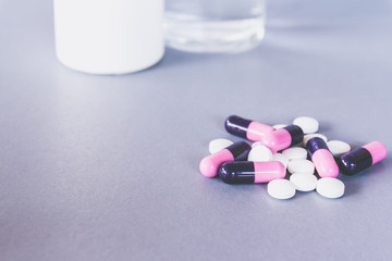 pills and tablets on grey background with bottle and glass