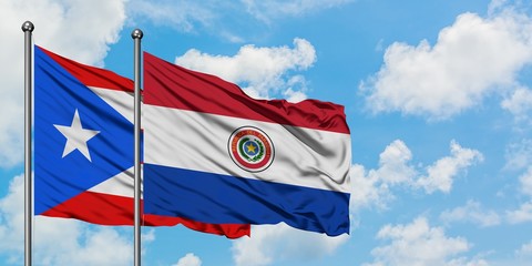 Naklejka premium Puerto Rico and Paraguay flag waving in the wind against white cloudy blue sky together. Diplomacy concept, international relations.
