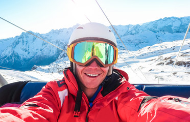 Happy snowboarder taking selfie photo with smartphone camera sitting on ski lift - Young man having...