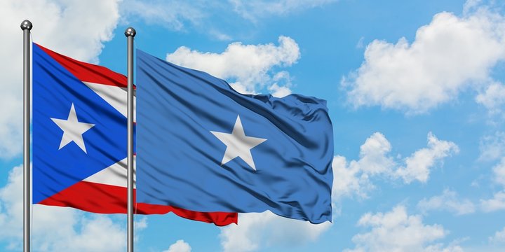 Puerto Rico and Somalia flag waving in the wind against white cloudy blue sky together. Diplomacy concept, international relations.