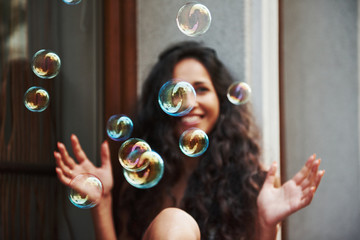 Cute girl plays with bubbles like a child. Beautiful woman with curly black hair have good time in...