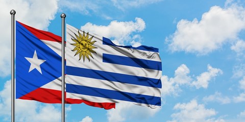 Puerto Rico and Uruguay flag waving in the wind against white cloudy blue sky together. Diplomacy concept, international relations.