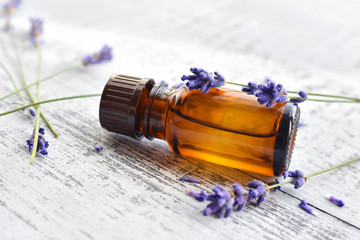 Organic lavender essential oil in dark glass transparent bottle and fresh lavender flowers on wooden background. Natural daylight, side view. Aromatherapy treatment.