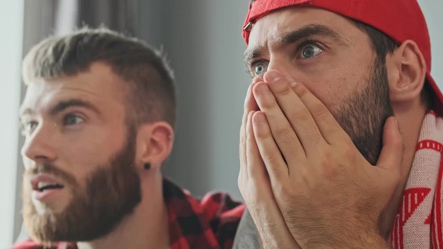 Two surprised bearded male fans getting shock while watching sport at apartment