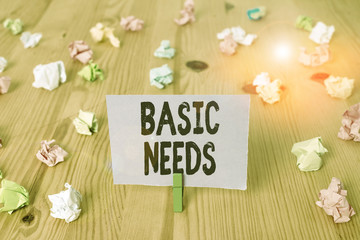 Writing note showing Basic Needs. Business concept for something that you must have in order to sustain or live life Colored crumpled papers wooden floor background clothespin