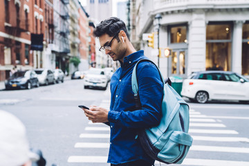 Ethnic young man using smartphone on street while walking