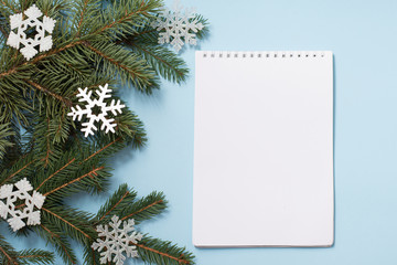 Note book with Wish List. Snowy fir branches on blue background, copy space. Christmas and winter concept.