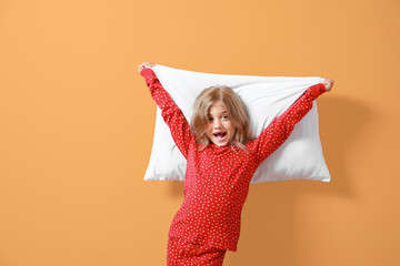 Happy little girl in pajamas and with pillow on color background