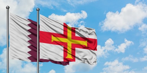 Qatar and Guernsey flag waving in the wind against white cloudy blue sky together. Diplomacy concept, international relations.