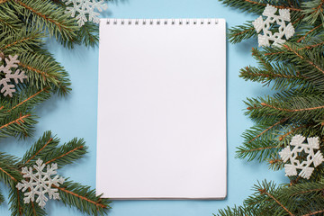 winter blue background with white note pad with wish list, christmas tree and snowflakes. copy space