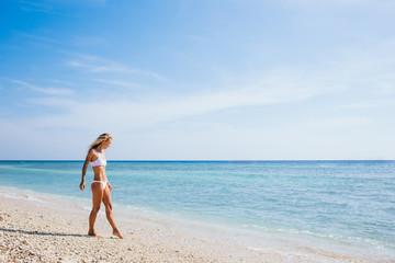 Fototapeta na wymiar Young slim woman walking along seashore