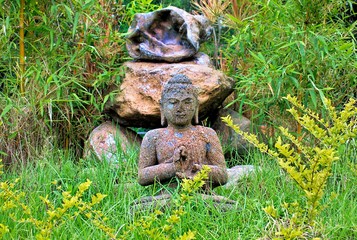 Cement made Buddha Statue among green grass and bamboo trees in garden 