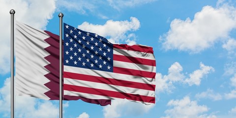 Obraz premium Qatar and United States flag waving in the wind against white cloudy blue sky together. Diplomacy concept, international relations.