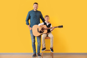 Handsome man and his little son with guitar near color wall