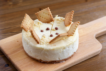 A whole of classic New York cheesecake decorated with square cookies on plate, on wooden table in coffee pastry shop. Cake sweet dessert for holiday, birthday party. Cheesecake for the celebration clo