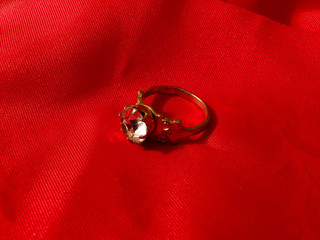 Gold ring with a large diamond on a red silk fabric close-up. Wedding ring for a wedding, anniversary or just a gift to a woman. Ring of gold with a precious stone.