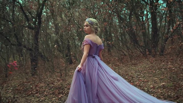 beautiful young blonde princess walks in purple lush dress with a long train. Frightened, lost in forest. Glamorous woman queen in crown. Autumn backdrop with orange leaves. Medieval vintage fashion