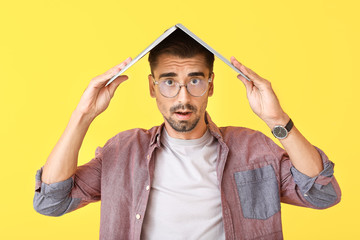 Stressed man with laptop on color background