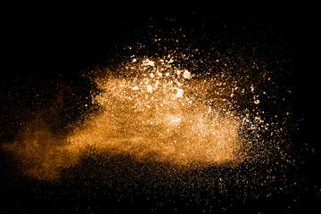 Fototapeta na wymiar abstract orange powder explosion on black background. Freeze motion of orange dust splash. Painted Holi powder.