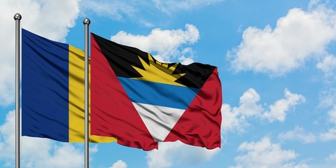 Romania and Antigua and Barbuda flag waving in the wind against white cloudy blue sky together....