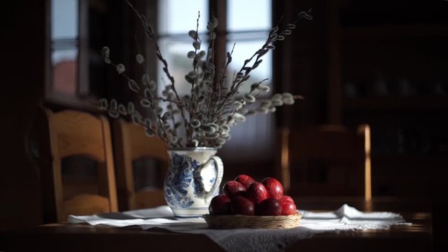 Camera panning and close up of Easter decoration: traditionally painted eggs and catkins in a hand made vase and hand made table cloth on the dining table