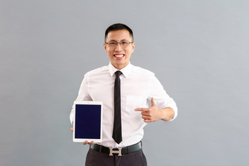 Asian businessman with tablet computer on grey background