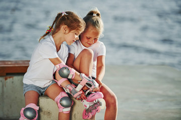 Two little girls with roller skates outdoors near the lake at background