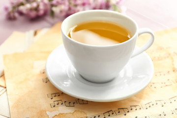 Cup of hot tea with music sheets on table